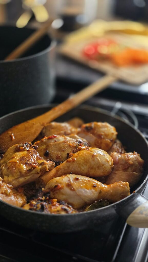 Close-up of seasoned chicken drumsticks sizzling in a pan, perfect for a home-cooked meal.