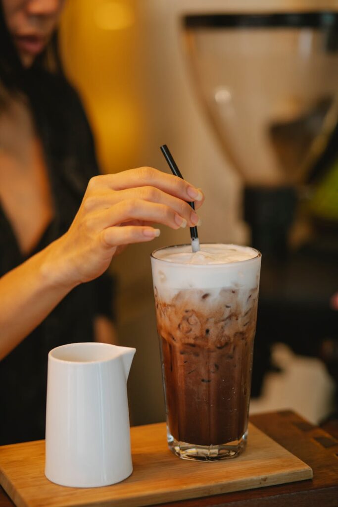 Refreshing iced coffee topped with frothy cream, stirred in a cozy café setting.