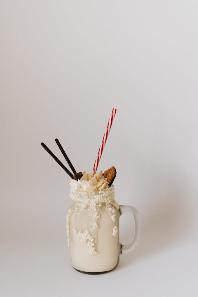A delectable milkshake in a glass mug, topped with cookies and straws on a white background.