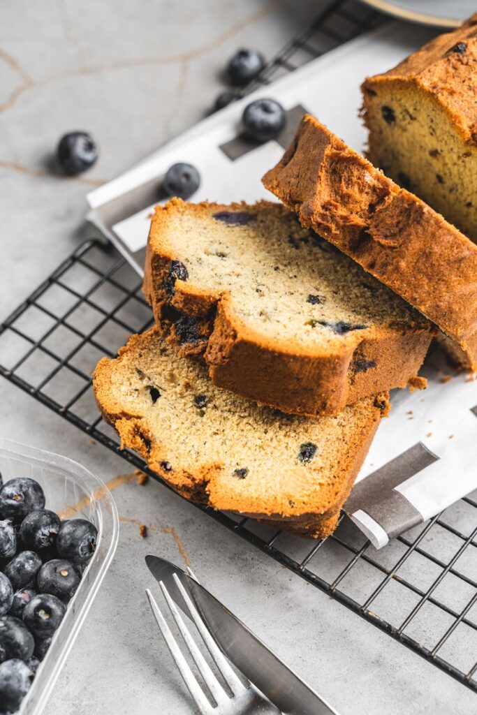 Close-up of sliced blueberry bread on a cooling rack with fresh blueberries.