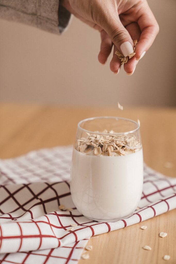 Hand sprinkling oats into a fresh milk smoothie, perfect for a healthy breakfast.